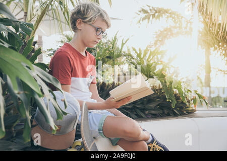 Jugendlich liest ein Buch im Freien. Junge Junge, sitzen in einem exotischen Garten, Hausaufgaben glücklich und sorgenfrei. Porträt einer wunderschönen Studenten ein Studium an der Stockfoto