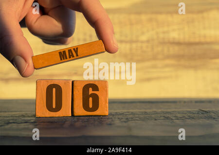 Am 6. Mai. 6. Tag des Monats, Kalender auf einem holzwürfel. die Hand einer Frau wird der Name des Monats auf die Zahl des Monats auf einer hölzernen Hintergrund Frühling Stockfoto