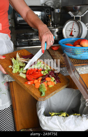 Detail einer weiblichen Hand Entsorgung der organischen Abfälle in einem geeigneten Behälter mit Küche im Hintergrund Stockfoto