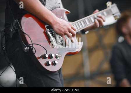 Ein erfahrener Musiker in Jeans und T-Shirt führt auf der Bühne und spielte einen schönen maroon E-Gitarre. Stockfoto