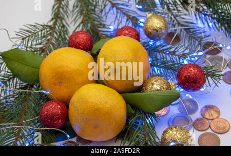 Tangerinen, Weihnachtsschmuck und Münzen verschiedener Länder liegen auf einem hellen Hintergrund. Stockfoto