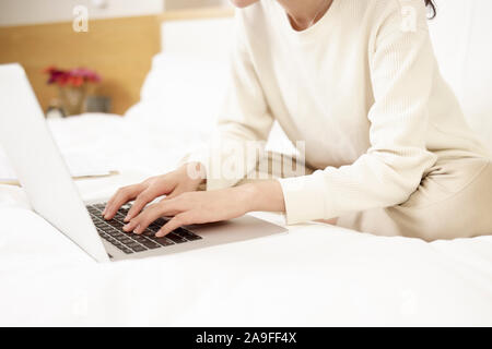 Junge asiatische Frau sitzt auf dem Bett arbeiten mit Laptop, auf Händen konzentrieren Stockfoto