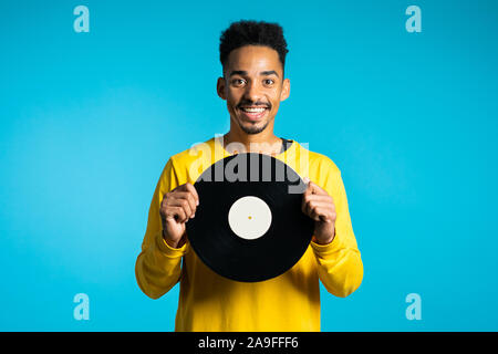 Junge schöne afrikanische amerikanische Mann in Gelb tragen Holding Schallplatten auf blauem Hintergrund. Retro Style Music Konzept. Stockfoto