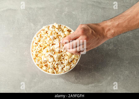 Männliche Hand und Schaufel mit Popcorn auf grauem Hintergrund, Ansicht von oben Stockfoto