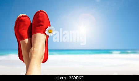 Beine mit rotem Tuch Schuhe und Blumen vor der Strand und das Meer. Stockfoto