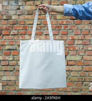 Weibliche Hand, die eine Tasche gegen Mauer tote, leeren Raum Stockfoto