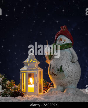 Schneemann Figur und leuchtenden Laternen auf Schnee mit einer sternenklaren Nacht Himmel Hintergrund Stockfoto