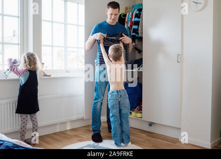 Vater, der sein Kind Hilfe erhalten, morgens bereit für die Schule angezogen Stockfoto
