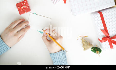 weihnachtssegenskonzept und Happy New Year. Mann mit weißem Pullover, der schreibt und eine Grußkarte schickt. Stockfoto