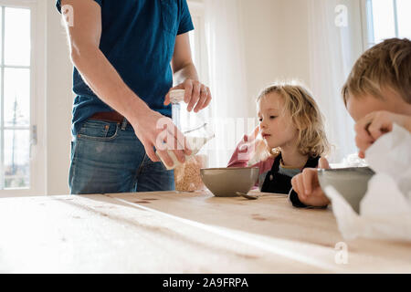 Vater helfen, die Kinder mit ihrem Frühstück am Morgen zu Hause Stockfoto