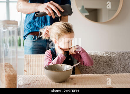 Vater Bürsten seine Töchter Haar am Frühstückstisch vor der Schule Stockfoto