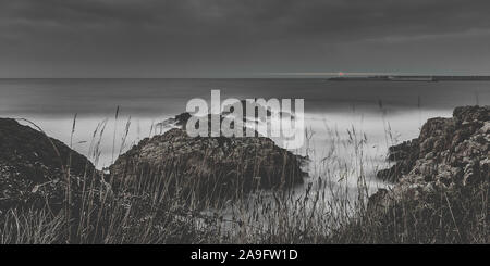 Lange Belichtung Bild mit Felsen und seidigen Wasser der Küste bei Nacht. Stockfoto