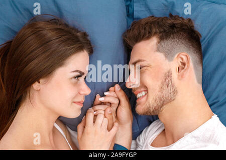 Bedtime. Junges Paar liegend auf Bett Draufsicht Hände halten sich einander glücklich close-up Stockfoto