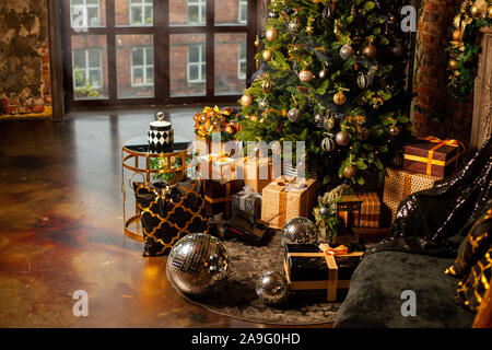 In der Nähe eines Weihnachtsbaumes mit goldenen Kugeln dekoriert. Unter dem Weihnachtsbaum eine große Anzahl der Weihnachtsgeschenke. Weihnachten Konzept. Eine riesige Stockfoto