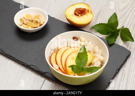 Porzellan Schüsseln mit sorghum Porridge, Pfirsich, Cashewnüsse, Mandel- und Minze auf Stein. Vegan glutenfrei Hirse Salat mit frischen Früchten. T Stockfoto