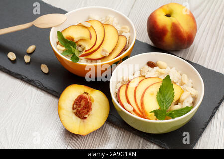 Porzellan Schüsseln mit sorghum Porridge, Pfirsich, Cashewnüsse, Mandel- und Minze, Löffel aus Holz auf Stein. Vegan glutenfrei Hirse Salat mit f Stockfoto