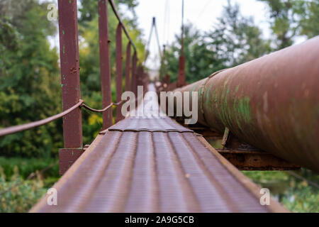 Einen schmalen alten rostigen River Crossing, zusammen mit einer Wasser- und Gasleitung. Kommunikation im Dorf Stockfoto