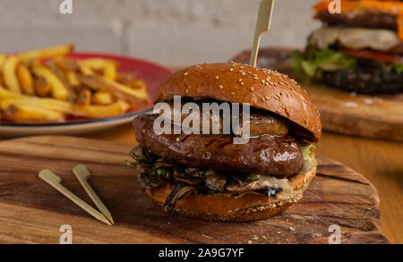 Leckere hausgemachte Hamburger mit Foie poilé, Pilze, Salat und Soße auf Holzbrett Stockfoto