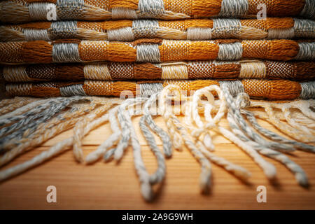 Gestapelte gestrickt Plaid mit Fransen. Strick Decke Stoff Textur mit einer komplexen Square verweben. Stockfoto