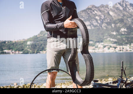 Fahrrad reparieren. Mann Instandsetzung Mountainbike. Radfahrer Mann in Schwierigkeiten hinten Wheel bei Unfall. Mann Bike in der Nähe von See in Italien Hintergrund Stockfoto