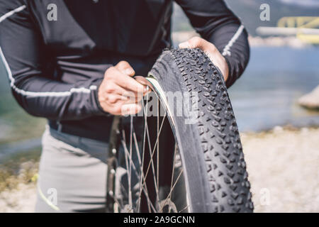 Fahrrad reparieren. Mann Instandsetzung Mountainbike. Radfahrer Mann in Schwierigkeiten hinten Wheel bei Unfall. Mann Bike in der Nähe von See in Italien Hintergrund Stockfoto