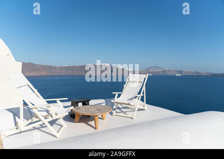 Zwei weiße Liegestühle auf weißen Dachterrasse mit Blick auf das Mittelmeer auf der griechischen Insel Santorini. Stockfoto