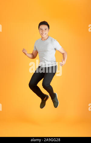 Energetische glückliche junge asiatische Mann in Freizeitkleidung springen, Studio shot orange Hintergrund isoliert Stockfoto