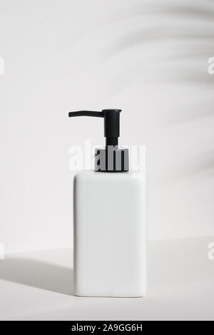 Leere weiße kosmetische Flasche mit einem tropischen Blatt auf weißem Hintergrund Stockfoto