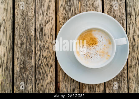 Schaumbildung Espresso mit Milch in eine weiße ceramich Schale auf eine Untertasse steht auf einem Holztisch und sieht lecker. Ansicht von oben, Makro mit Kopie Raum Stockfoto