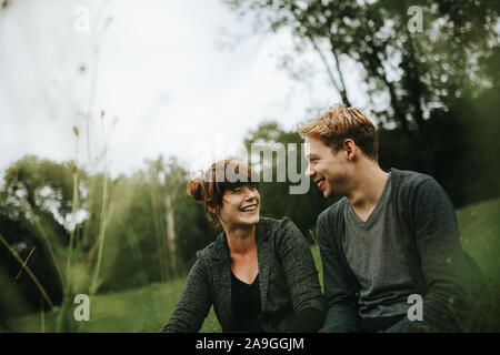 Junge heterosexuellen Paaren, im Gras sitzen lächeln Stockfoto