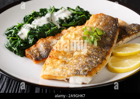 Lecker gegrilltes Barschfilet mit Spinat und Zitrone close-up auf einem Teller auf den Tisch. Horizontale Stockfoto