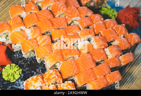 Philadelphia Grün sushi Rollen aus frischem Lachs, Frischkäse, Gurke, Avocado. Mit Ingwer und Wasabi (japanischer Meerrettich) auf schwarz serviert. Stockfoto