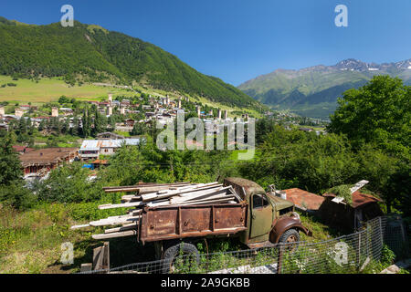 Mestia Georgien - Juli 29, 2019; Dorf Mestia mit alten Lastwagen und typische Swanetien Türme mit kaukasischen Bergblick Hintergrund während des Tages i Stockfoto