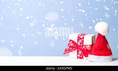 Kleine weiße Geschenkbox mit roter Schleife und Santa Claus hat im Schnee auf blauem Hintergrund. Weihnachten banner Mockup, Neues Jahr Grußkartenvorlage. Stockfoto