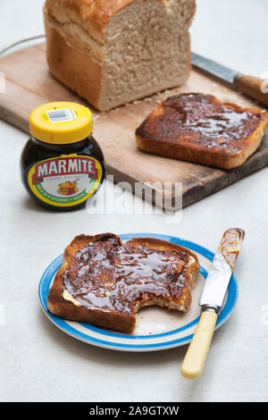 Marmite auf Toast auf einem Schild neben einem Laib Weißbrot und ein Glas marmite Stockfoto