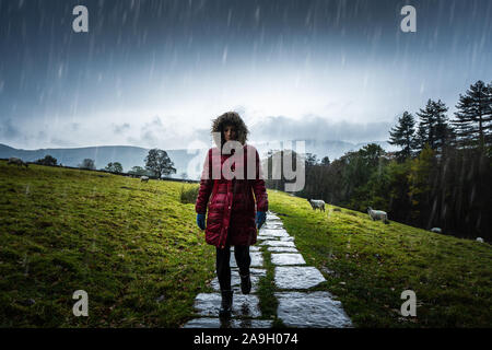 Eine junge Frau, Wanderer, einen Berg klettern im kalten Winter Regen in der Derbyshire Peak District National Park, in der Wintersaison in der britischen Landschaft Stockfoto