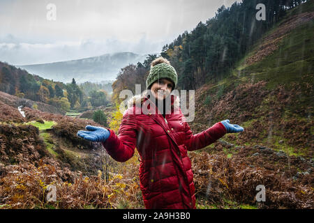Eine junge Frau, Wanderer, Kletterer nimmt einen Bruch von einen Berg klettern und posiert für ein Foto beim Stehen im kalten Winter regen Stockfoto
