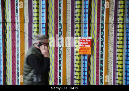 Ein Mann auf seinem Handy an eine Sozialistische Arbeiter Poster in der Nähe von Ladbroke Grove tube station in Notting Hill, London. Das Plakat liest: "Tories haben Blut an ihren Händen Gerechtigkeit für Grenfell'. Stockfoto