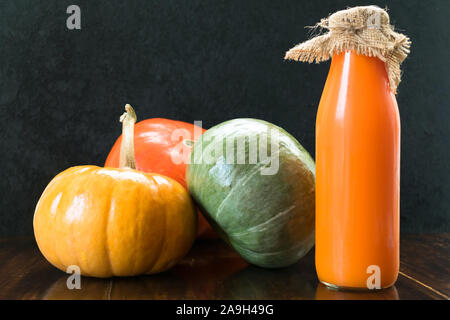 Kürbis Saft in eine Flasche und drei verschiedene Kürbisse auf einem schwarzen Hintergrund. Close-up. Stockfoto