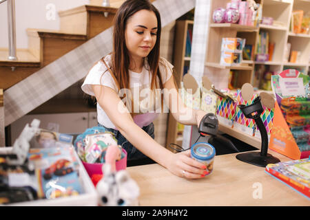 Junge kaukasier weiblich Frau Kassierer in Toy Store. Frau verwenden Kassierer Zähler in kids Mall. Stockfoto