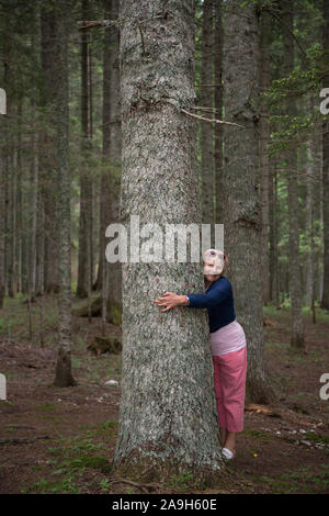 Im Alter von lächelnde blonde Frau ist das Umarmen großen Baumstamm im Nationalpark Durmitor in der Nähe von Zabljak Stadt, Montenegro. Stockfoto