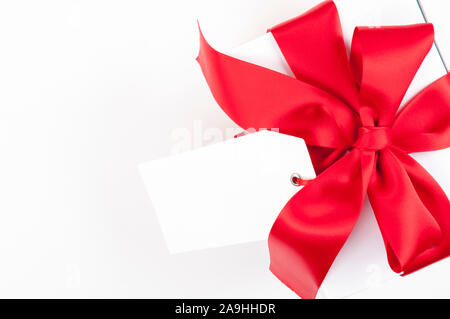 Leere Geschenk Tag hing ein Geschenk Box mit rotem Satinband auf weißem Hintergrund Stockfoto