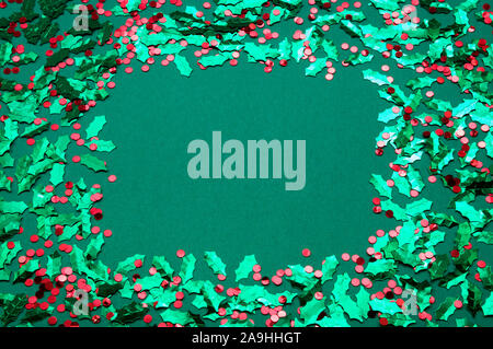 Urlaub frame von leeren grünen Kopie Raum grenzt mit glänzenden besprüht von Blättern und roten Stechpalme Beeren Konfetti Stockfoto