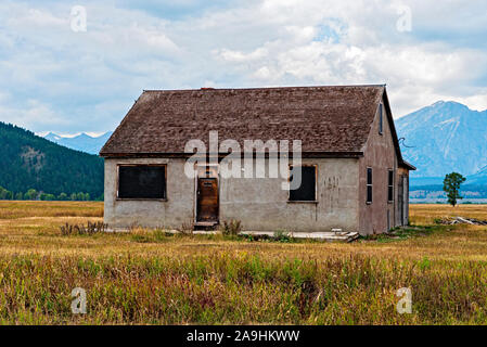 Altes verlassenes Pionierhaus auf goldenen Rasenfeldern mit Bergen jenseits des wolkenlosen Himmels. Stockfoto