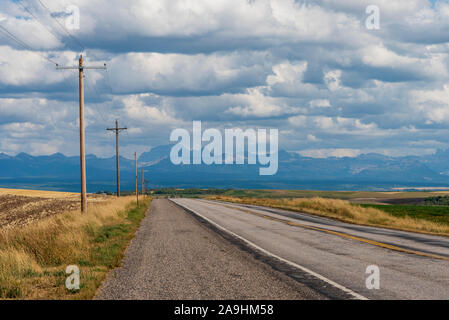 Blick auf die Autobahn vom Schotterroden mit Strompfosten und Weizenfeldern unter bewölktem Himmel. Stockfoto