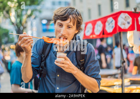 Junger Mann touristische Essen typisch koreanischen Street Food auf der Walking Street von Seoul. Würzig fast food einfach gefunden bei Koreanischen martket, Seele Korea Stockfoto