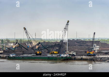 Lange Tau Fluss, Vietnam - 12. März 2019: Phuoc Khanh. Kohle Hafen mit Kais und seine Hügel des schwarzen Sachen. Hohe Kran und Pumpen Lkw unter Stockfoto