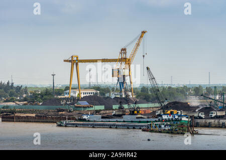 Lange Tau Fluss, Vietnam - 12. März 2019: Phuoc Khanh. Kohle Hafen mit Kais und seine Hügel des schwarzen Sachen. Hohe Kran und Schiffe entladen Stockfoto