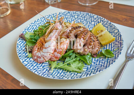 Gemischte gegrillte Meeresfrüchte einschließlich Thunfisch Steak und Schrimps Tintenfisch und Salat serviert auf einem modernen gedeckten Tisch Stockfoto