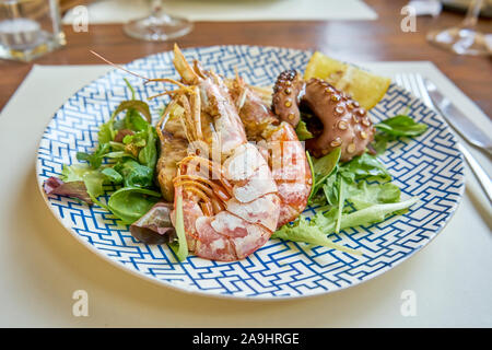 Gemischte gegrillte Meeresfrüchte einschließlich Thunfisch Steak und Schrimps Tintenfisch und Salat serviert auf einem modernen gedeckten Tisch Stockfoto